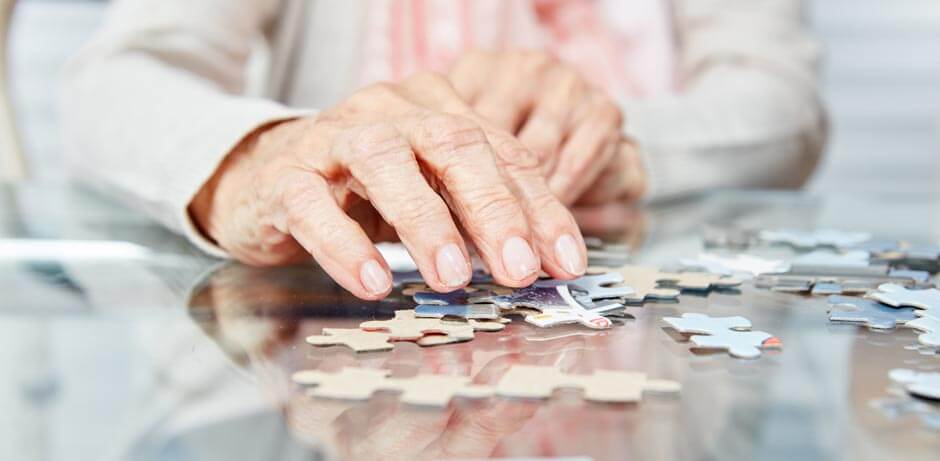 Hand einer älterer Person mit Puzzleteilen